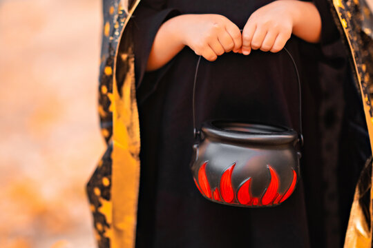 Halloween kids. Little girl in witch hat with candy bucket Close up, Toddler kid in witch costume playing in autumn park. A Child in a carnival costume outdoors 