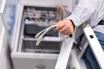 Male worker configures local network by holding cables and plugs to connect to server.