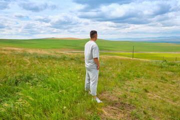 A man in light-colored clothes stands on the cliff of a hill and looks towards the Buryat Selenga River near the city of Ulan-Ude