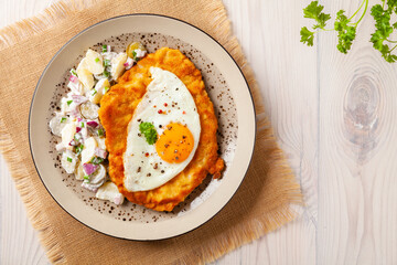 Viennese pork schnitzel with a fried egg. Served on potato salad. Natural wooden planks in the...