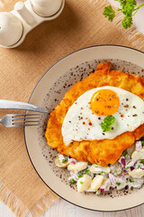 Viennese pork schnitzel with a fried egg. Served on potato salad. Natural wooden planks in the background.