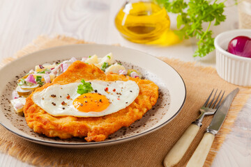 Viennese pork schnitzel with a fried egg. Served on potato salad. Natural wooden planks in the background. - obrazy, fototapety, plakaty