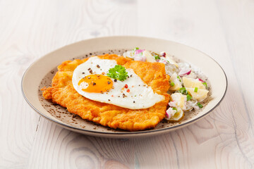 Viennese pork schnitzel with a fried egg. Served on potato salad. Natural wooden planks in the background.
