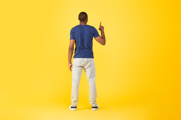 African Man Pointing Finger Up Over Yellow Background, Back View