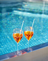 Close up of glasses with summer cocktails standing under scorching sun near poolside.
