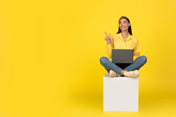 Happy Woman Using Laptop Pointing Finger Aside Over Yellow Background