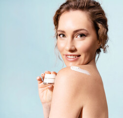 Pretty mid adult woman holding mock up jar of anti-ageing cream or serum. Happy female with cosmetic product on naked shoulder enjoying daily skincare routine for skin rejuvenation, natural beauty.