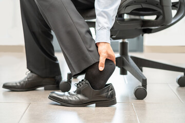 Closeup of business man touching feet with his hand at office