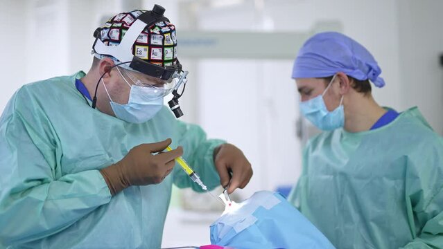 Performing nasal operation in modern clinics. Male surgeon in device glasses uses syringe in nose of a patient.