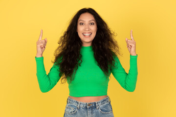 Cheerful Middle Eastern Woman Pointing Fingers Upward Over Yellow Background