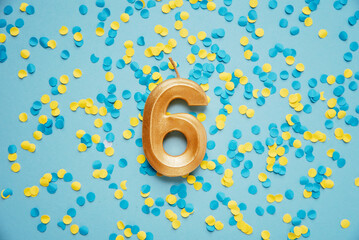 Number 6 six golden celebration birthday candle on yellow and blue confetti Background. Six years...