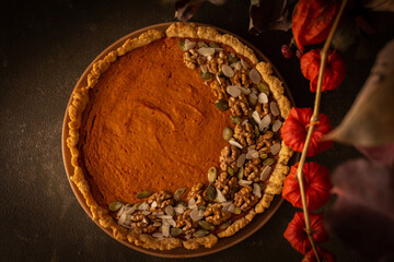 Musk gourd pie garnished with seeds, almond petals and walnuts, autumn table with pumpkins, dried flowers in a vase and a pie