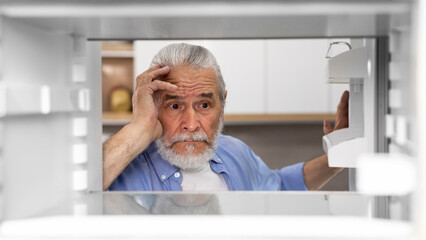 Fototapeta premium Portrait Of Hungry Elderly Man Searching For Food In Empty Fridge