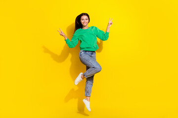 Fototapeta na wymiar Full length photo of lovely young girl jumping show double v-sign hello dressed trendy green sweatshirt isolated on yellow color background