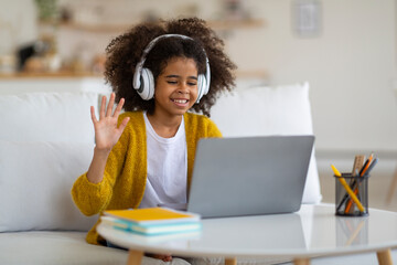 Positive black school girl using laptop, learning foreign language online
