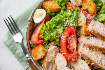 Healthy diet food. Chicken Caesar salad with chicken fillet, tomatoes, eggs, lettuce and cheese in a plate with fork. Top view