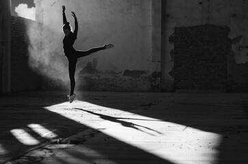 Ballerina jumping and dancing in an abandoned building on a sunny day in black and white