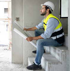 Engineer man reading blueprint as sitting at home improvement construction site. Professional architect wears safety hardhat is working on home interior, housing development project. Copy space.