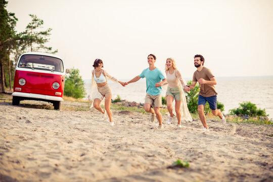 Photo of charming adorable hippie people company smiling running together holding arms outside seaside beach