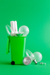 Saving electricity waste concept: diverse old halogen and fluorescent light bulbs in and around a recycling bin, green background, text or copy space.