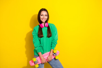 Photo of pretty satisfied girl toothy smile arms hold skateboard isolated on yellow color background