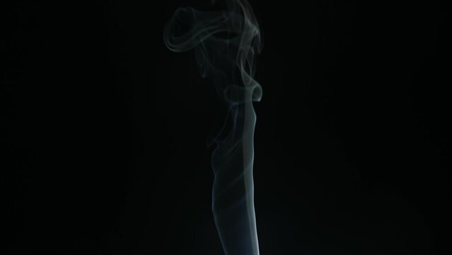 White smoke from incense stick flowing on black background