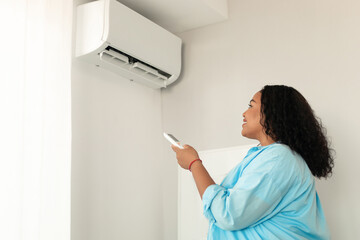 African American Woman Turning On Air Conditioner Standing At Home