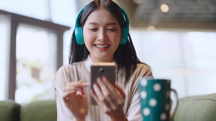 relax joyful casual asian female adult woman casual cloth enjoy listening music from streaming online playing music playlist application on smartphone via earphone on sofa couch at co working space   - Powered by Adobe