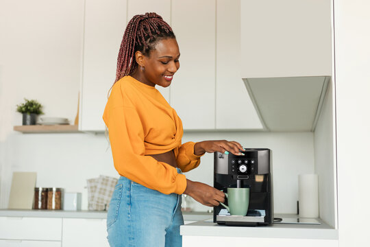 Excited Young Black Woman Making Fresh Aromatic Coffee In Modern Machine In Kitchen Interior