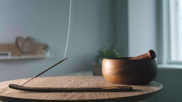 Holder with smoldering incense stick on wooden table in room