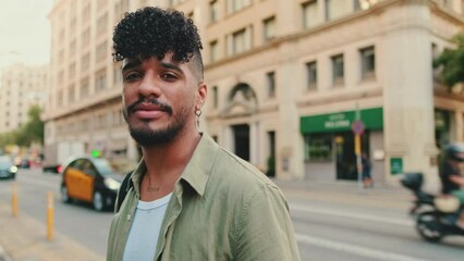 Close up, young happy man with beard dressed in an olive color shirt stands next to the road, turns his head and smiles at the camera - Powered by Adobe
