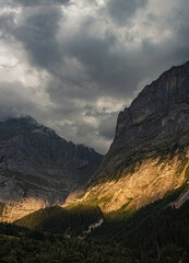 A valley under cloudy skies with warm sunshine lighting up part of the hillside