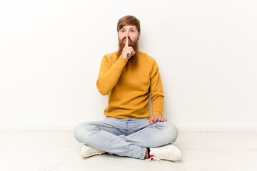 Young caucasian man sitting on the floor isolated on white background keeping a secret or asking for silence.