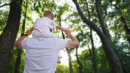 father and son in the park. dad carries his son on his neck a through the forest park glare of the sun outdoor recreation with children. happy family kid dream concept. father son piggyback lifestyle