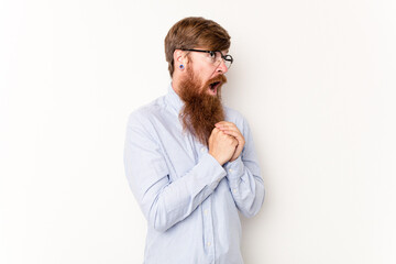 Young caucasian red-haired man isolated on white background praying for luck, amazed and opening mouth looking to front.