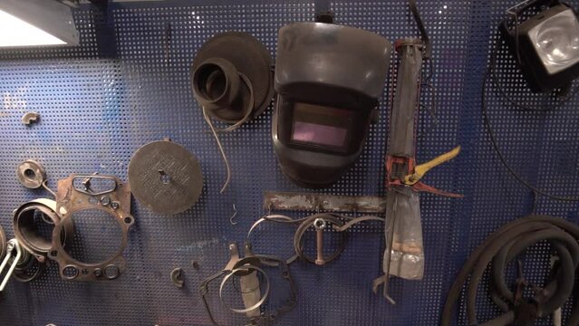 A set of various tools hanging on a vertical perforated panel in a car workshop. Car repair and maintenance tools on the wall in the garage, welding mask - a set of wrenches for removing the engine oi