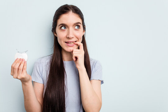Young caucasian woman holding teeth whitener isolated on blue background relaxed thinking about something looking at a copy space.