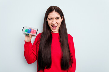 Young caucasian woman holding a batteries box isolated on blue background screaming very angry and aggressive.