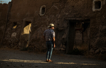 Obraz na płótnie Canvas Rear view of adult man in cowboy hat and shirt against abandoned building