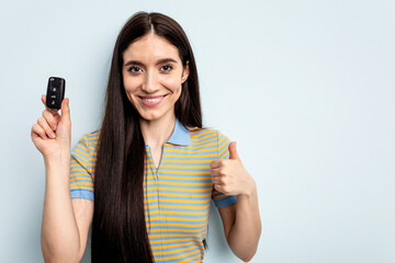 Young caucasian woman holding car keys isolated on blue background smiling and raising thumb up