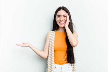 Young caucasian woman isolated on white background holds copy space on a palm, keep hand over cheek. Amazed and delighted.