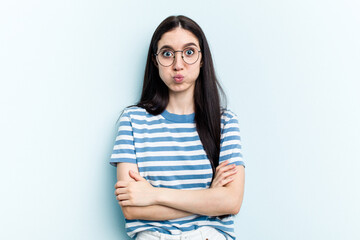 Young caucasian woman isolated on blue background blows cheeks, has tired expression. Facial...