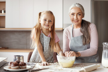 Granddaughter and grandma prepare cookies. Glad european little girl and elderly female in aprons...
