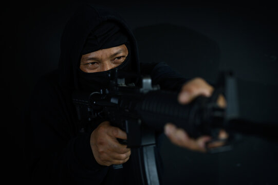 Armed terrorist in black balaclava mask aiming with automatic gun