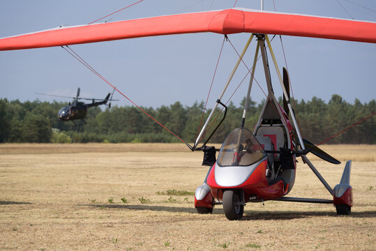 RECREATIONAL AND DISPOSABLE AVIATION - A Powered Hang Glider And Helicopter At A Field Airport