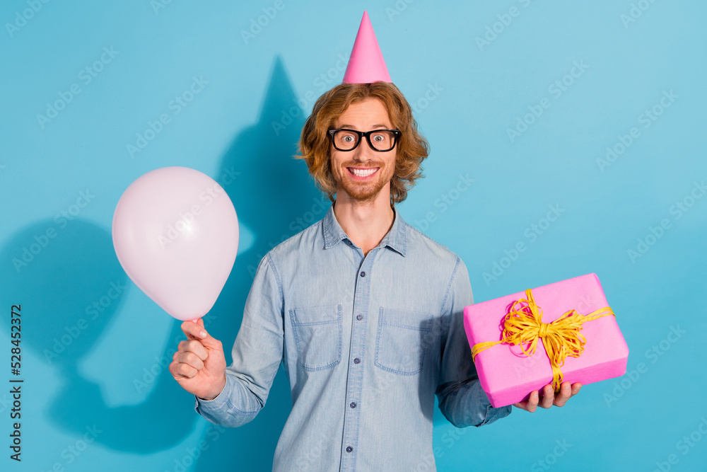 Sticker Photo of funny cute man wear denim shirt spectacles cap presenting gift balloon isolated blue color background