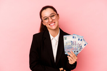 Young business caucasian woman holding bank notes isolated on pink background laughing and having fun.