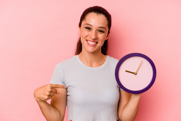 Young caucasian woman holding a clock isolated on pink background person pointing by hand to a...