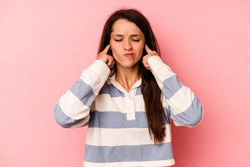 Young caucasian woman isolated on pink background covering ears with fingers, stressed and desperate by a loudly ambient.