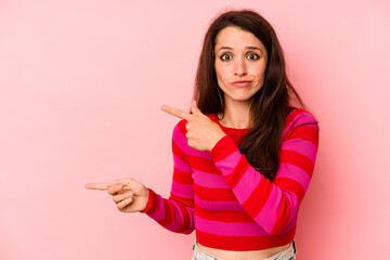 Young caucasian woman isolated on pink background shocked pointing with index fingers to a copy space.